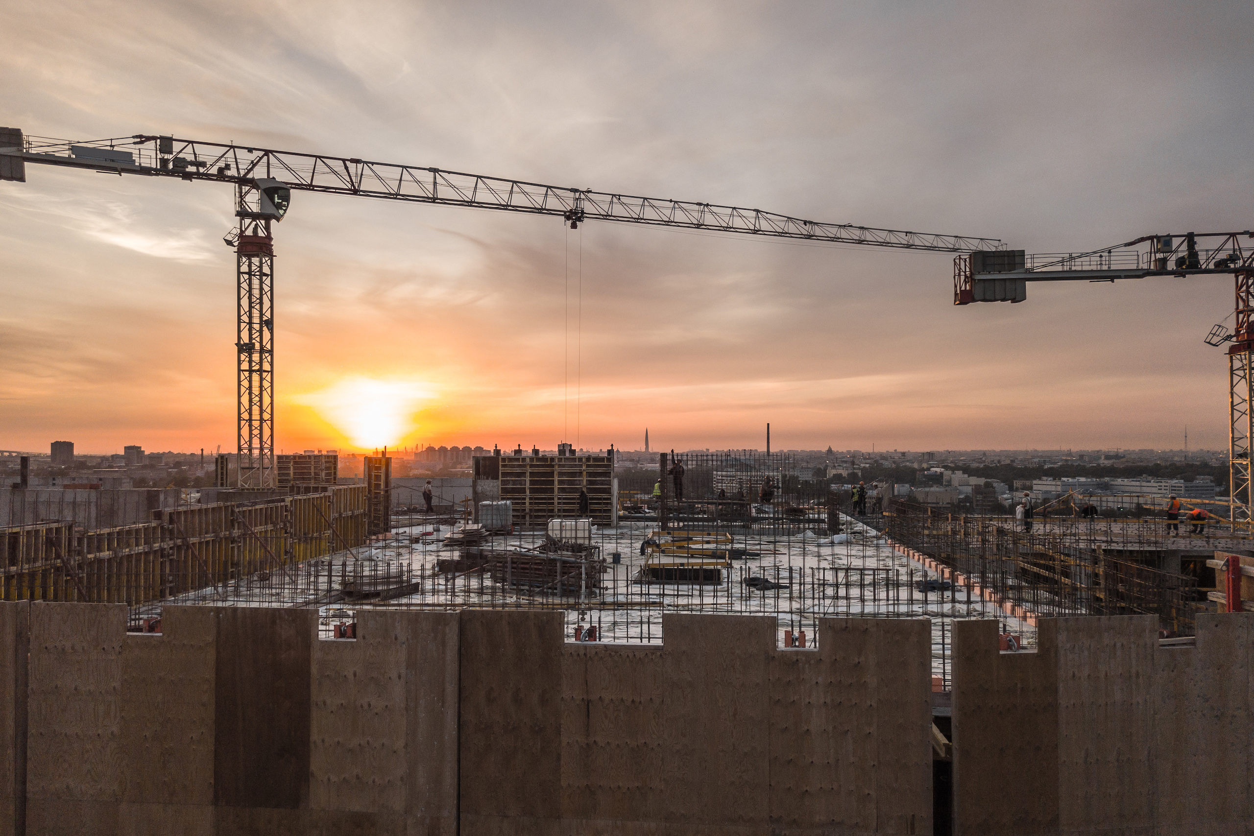 Cantiere edile in corso al tramonto, con gru e strutture in cemento armato